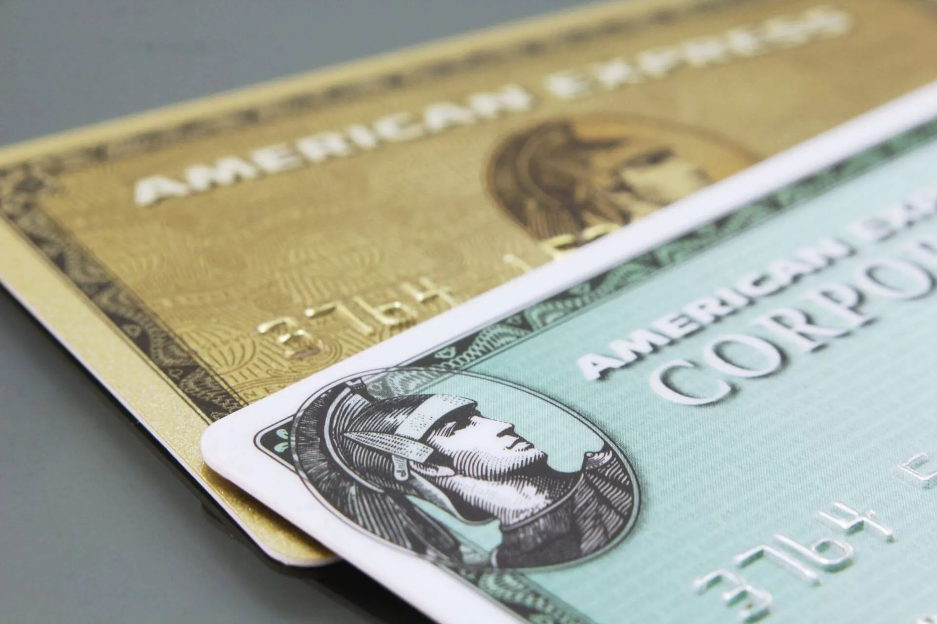 Close-up of three American Express credit cards stacked on a flat surface: gold, silver, and green in color, with embossed text and the company’s iconic centurion logo visible.