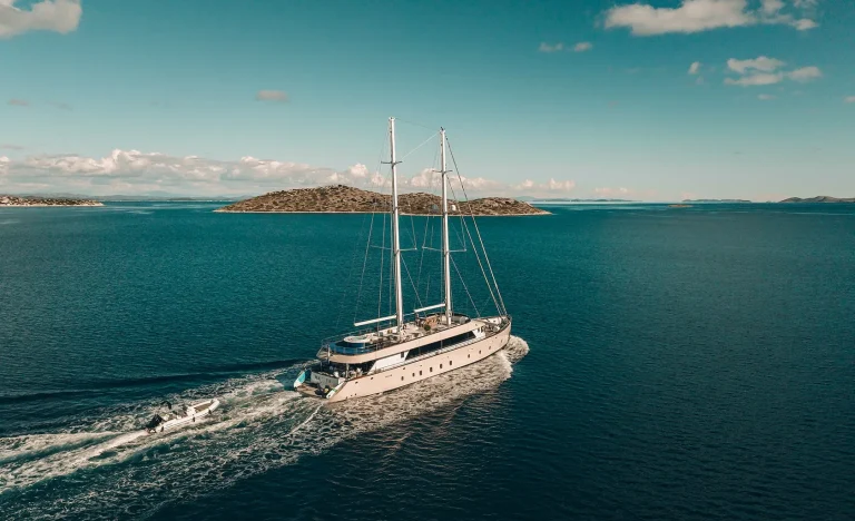 A large white yacht sails on calm blue water with small islands in the background under a partly cloudy sky.