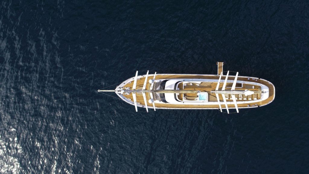 Aerial view of a large yacht with multiple decks floating on dark blue water, with sunlight reflecting off the surface beside the boat.