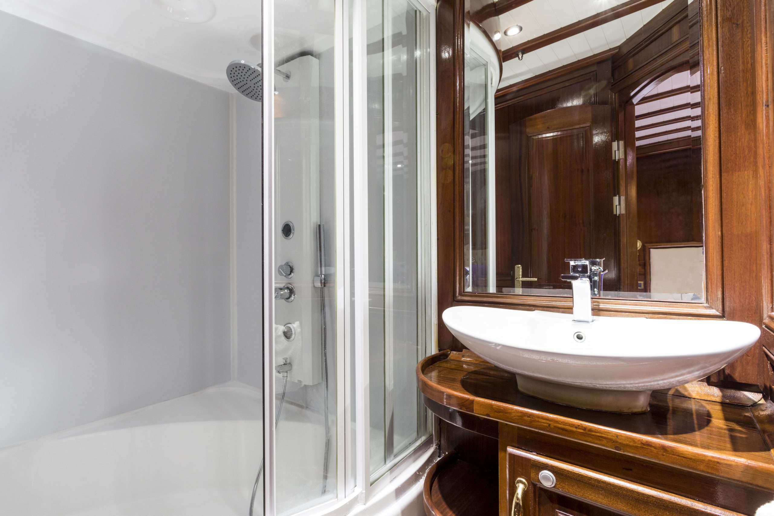 Modern bathroom with a glass-enclosed shower, a white vessel sink on a wooden vanity, and a wall-mounted mirror reflecting the wooden ceiling details.