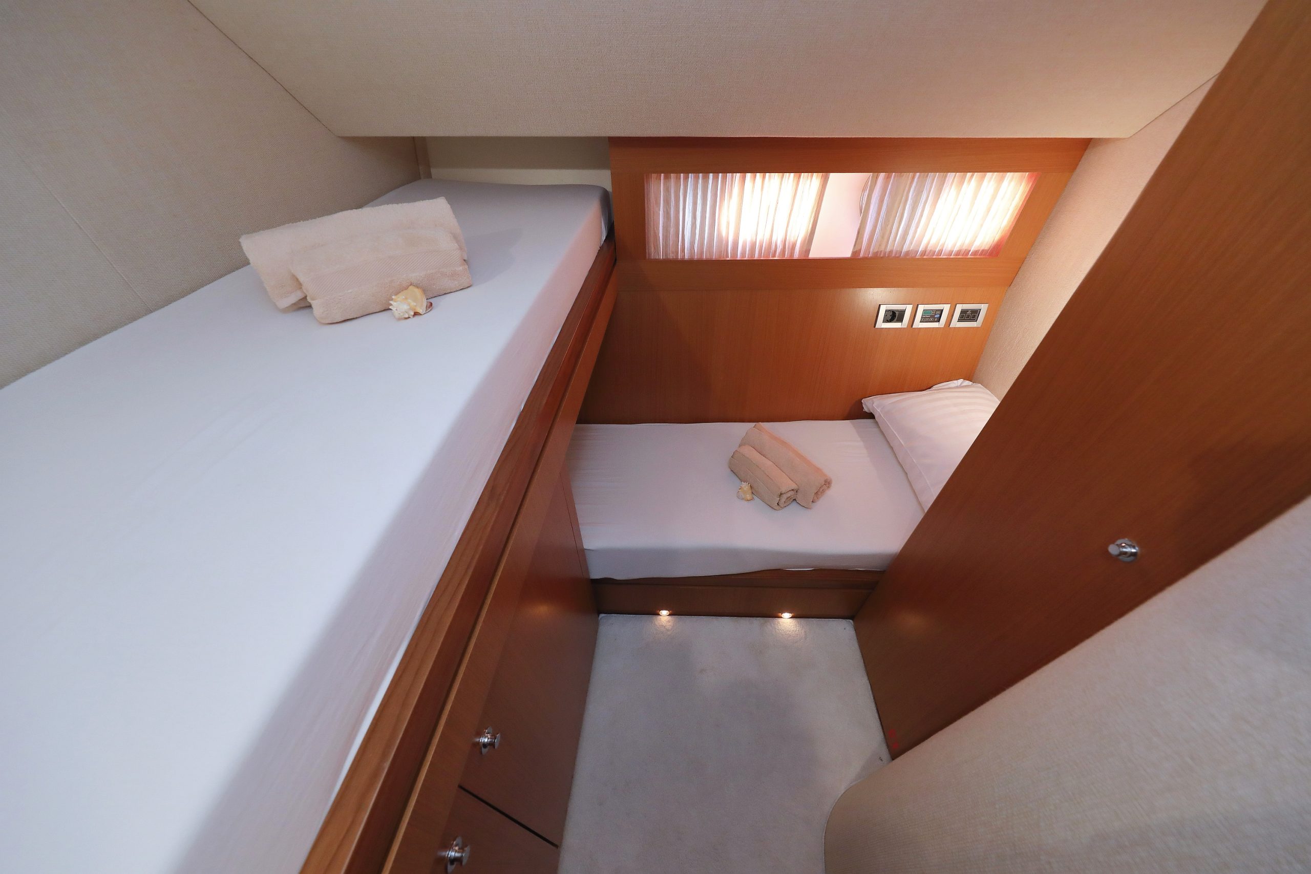 Un camarote pequeño y ordenado con dos camas individuales -una superior y otra inferior-, ambas con ropa de cama blanca y toallas dobladas. Los muebles de madera y la iluminación tenue crean un ambiente acogedor.