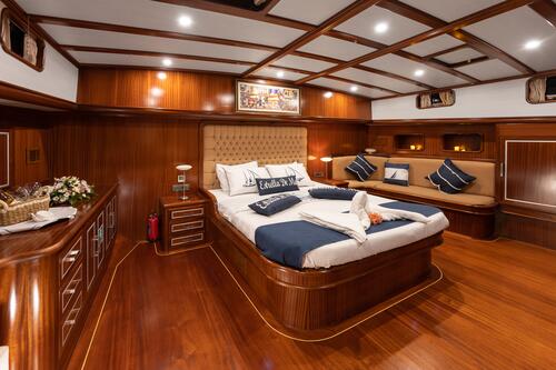 Luxurious yacht bedroom with polished wood paneling, a large bed with navy and white bedding, decorative pillows, a cushioned bench, built-in lighting, and nautical décor accents.