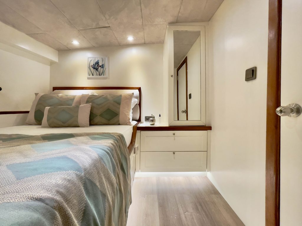 A modern, cozy bedroom with a double bed topped with patterned pillows and a geometric blanket, built-in nightstand and vanity with drawers, a wall mirror, soft lighting, and minimalist decor.