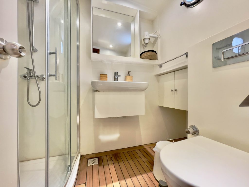 Modern bathroom with glass shower enclosure, wall-mounted sink, toilet, wooden floor, large mirror, and white cabinets. Minimalist decor with neutral tones and simple accessories.