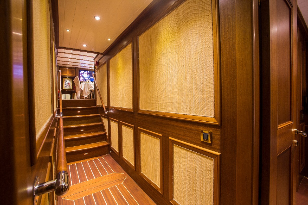 Un vestíbulo con suelos de madera y paredes paneladas conduce a una escalera. Una iluminación cálida y una decoración elegante crean un ambiente acogedor y de lujo. Al final de la escalera, se ve parcialmente una zona de estar con un cuadro.