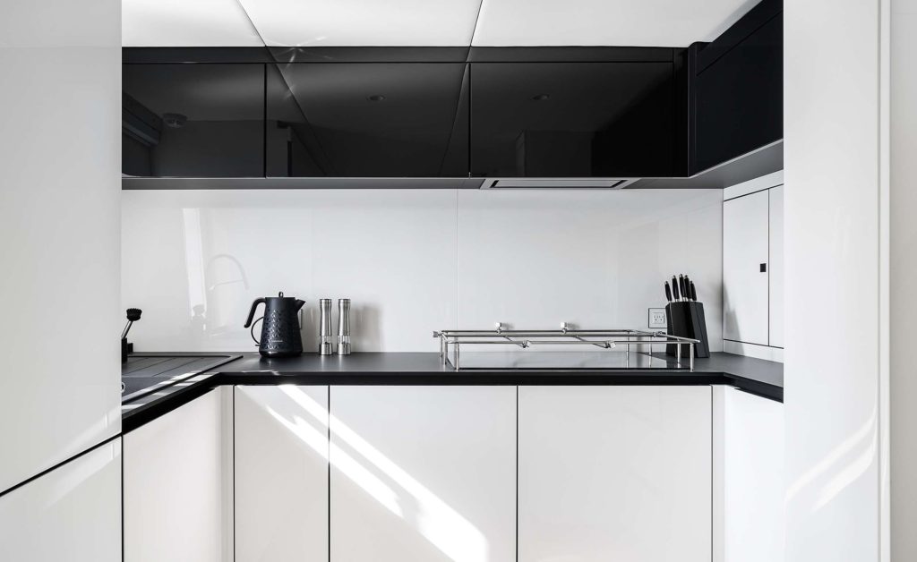 Modern kitchen with glossy white cabinets, black countertops, a kettle, knife block, spice mills, and a dish rack—styled with minimalism and natural light, perfect for a yacht charter or luxury yachts for charter experience.