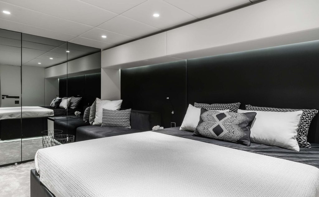 Modern bedroom with a large bed, monochrome decorative pillows, black accent wall, mirrored closet doors, and recessed lighting—offering sleek decor inspired by the elegance found on luxury yachts for charter.