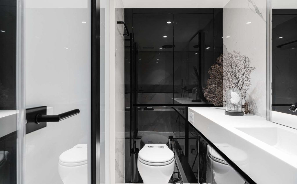 Modern bathroom with a minimalistic design featuring a white toilet, sleek sink, black accents, glass partition, and a decorative vase. The well-lit space evokes the elegance found in luxury yachts for charter.