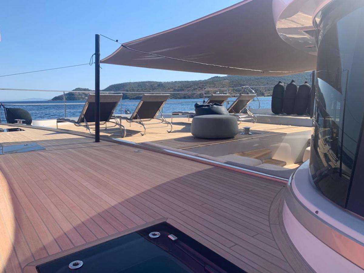 Spacious yacht deck with lounge chairs, sunshades, and a view of calm blue water and distant hills under a clear sky.