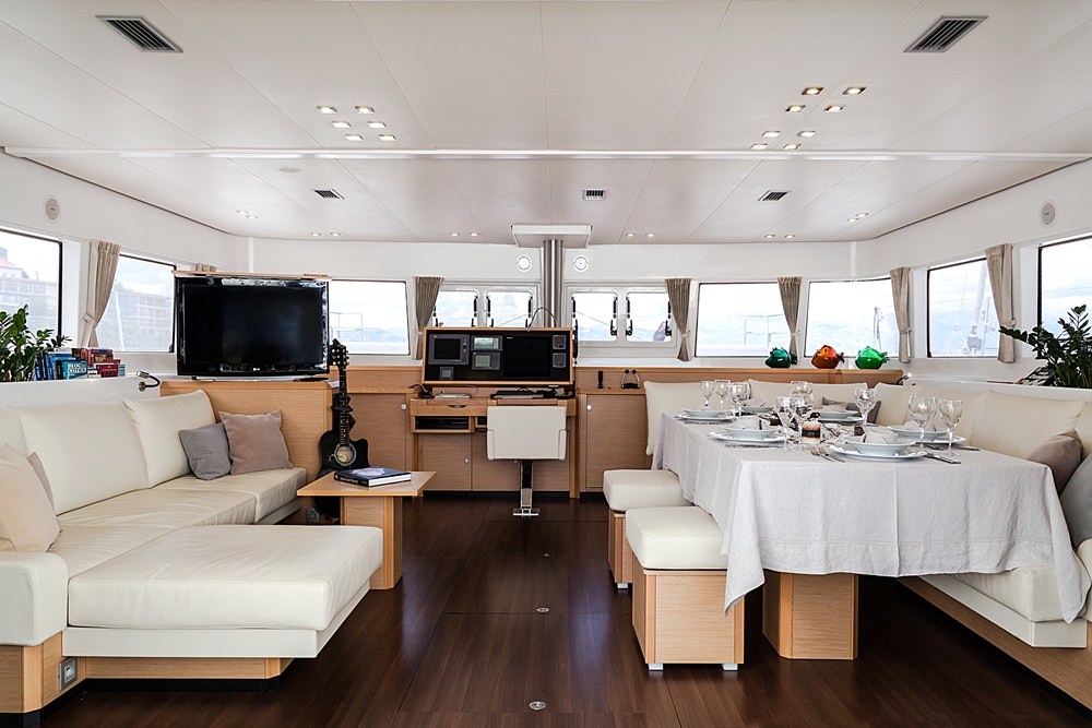 Modern yacht interior with cream-colored sofas, a dining table set for six, and large windows. Wood floors add warmth to this elegant space—perfect for a relaxing yacht charter experience.