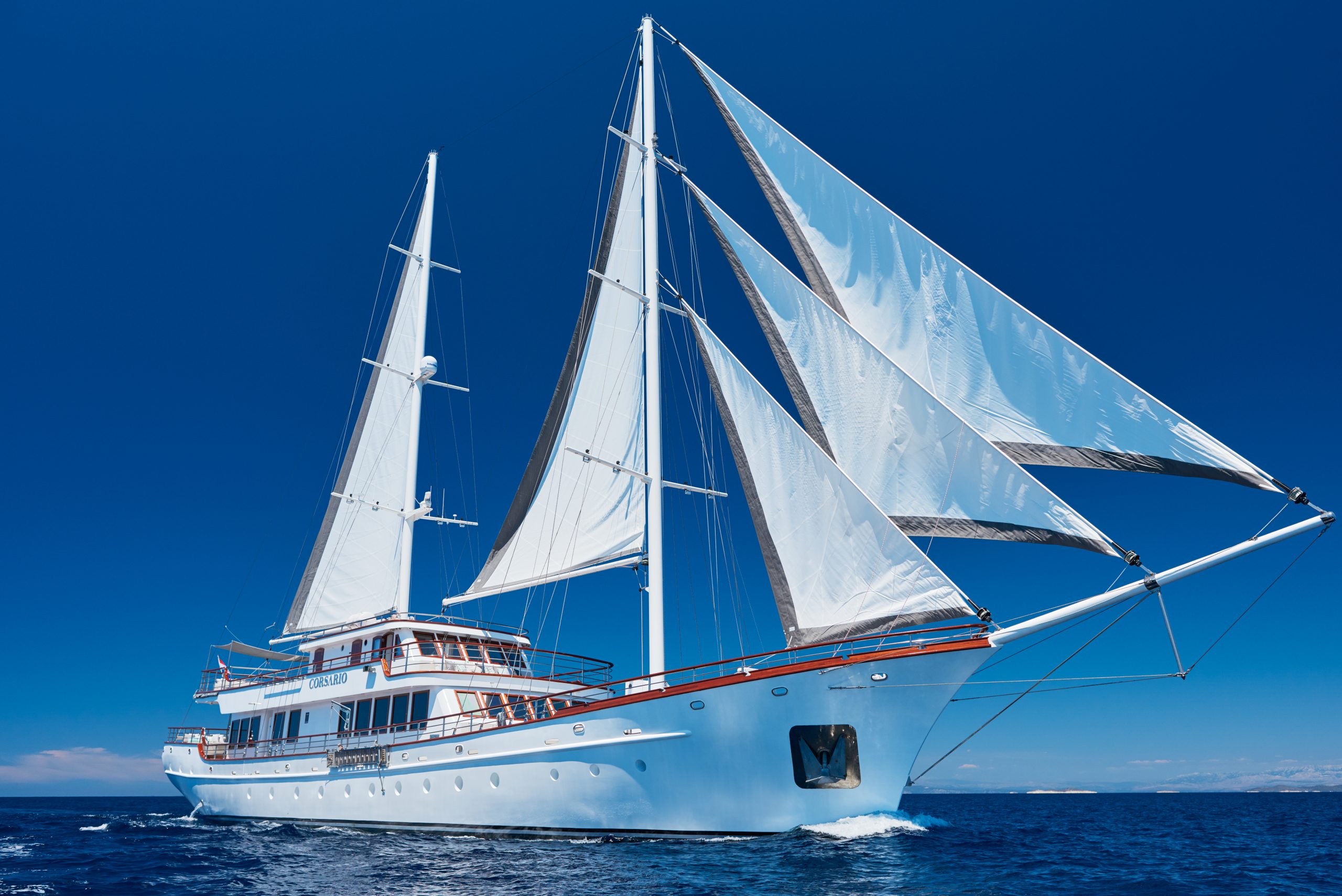 A large white sailing yacht with two masts and several sails open, cruising on calm blue water under a clear sky.