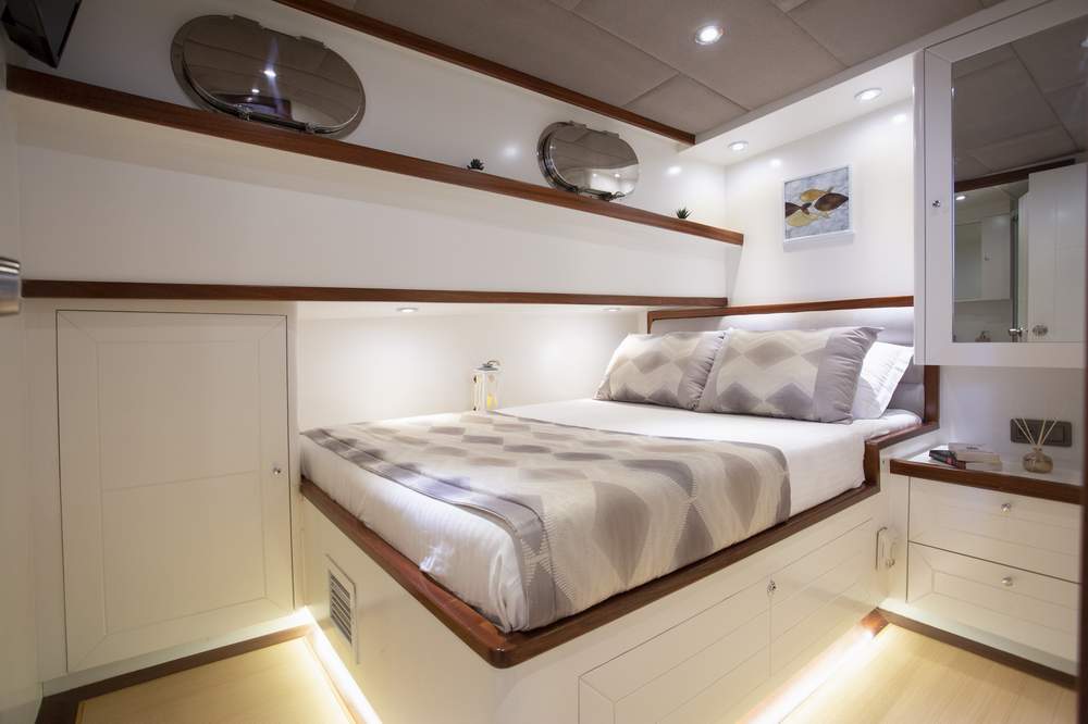 A modern, compact bedroom with a neatly made bed, white walls, built-in shelves, mirrors, soft lighting, and minimalist decor, creating a cozy and organized space.