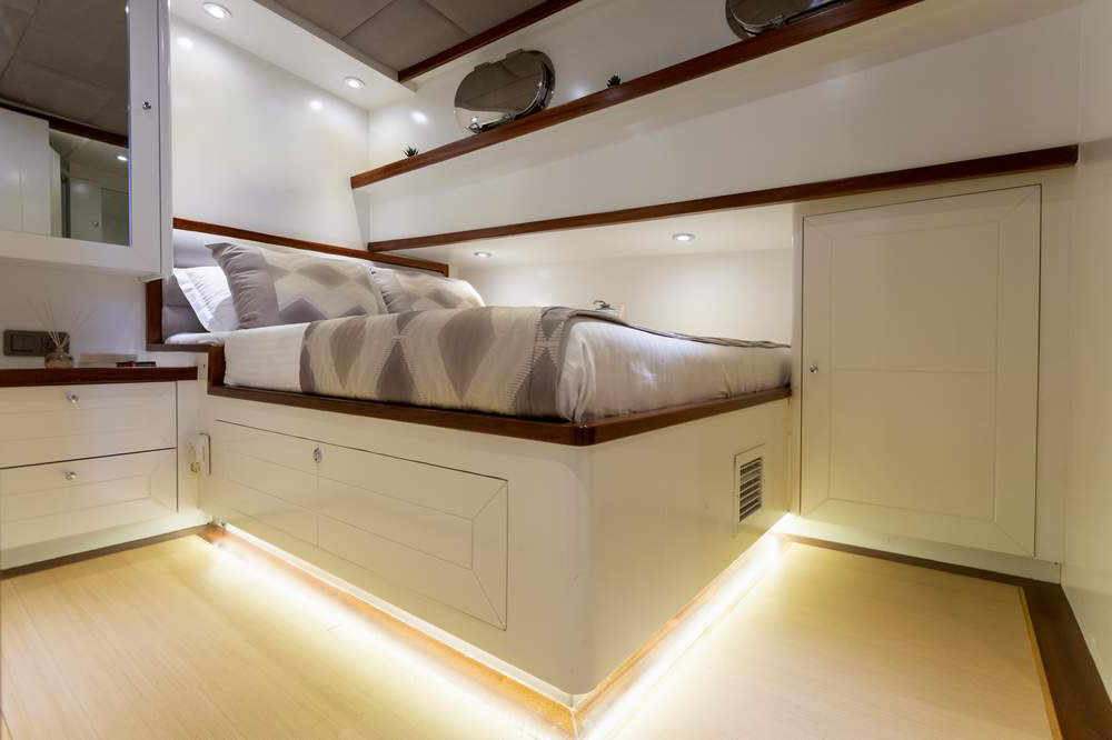 A modern, compact bedroom with a raised bed, white built-in cabinets, under-bed lighting, and neutral-colored bedding, creating a clean and cozy atmosphere.