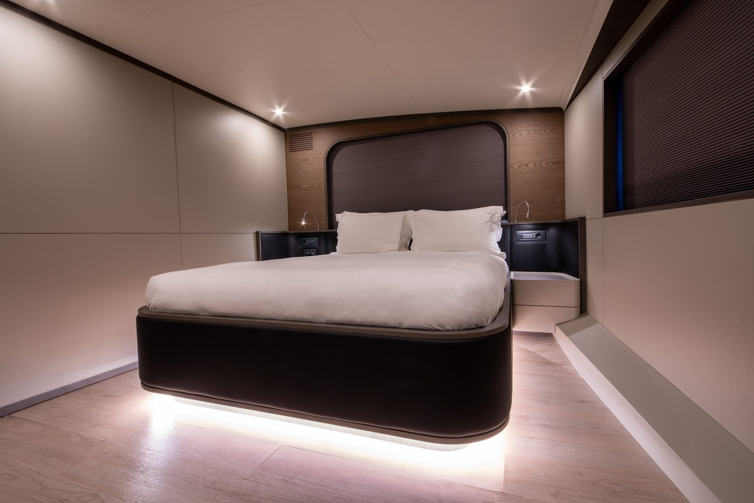GOOD LIFE A modern, minimalist bedroom with a floating double bed, white bedding, soft under-bed lighting, wood floors, and built-in nightstands, all illuminated by recessed ceiling lights.