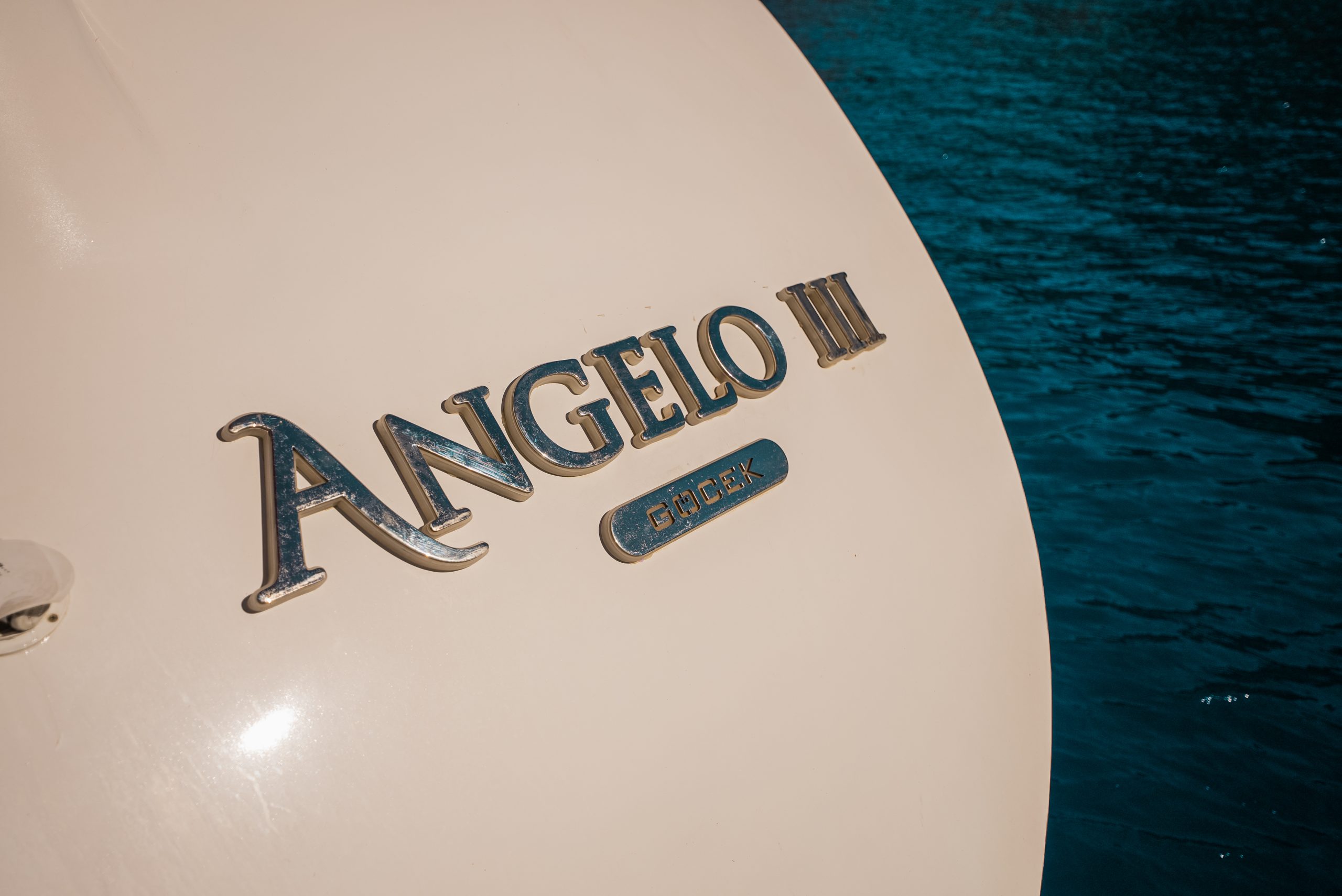 Close-up of a boat’s hull with the name ANGELO III and a GIODEX plaque, set against deep blue water—perfect inspiration for your next yacht charter adventure.