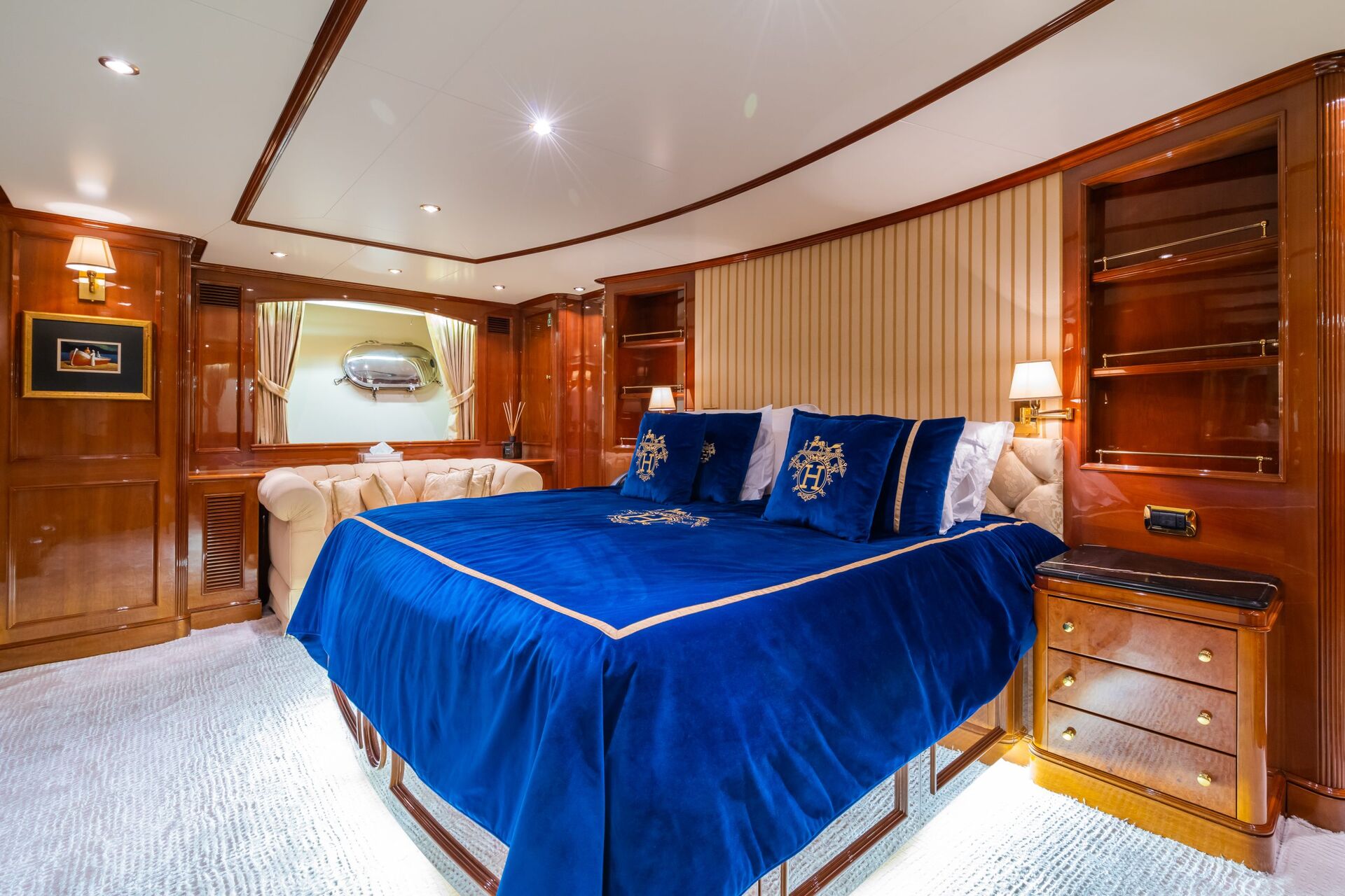 Luxurious bedroom with a large blue velvet bed, gold accents, built-in wooden cabinets, a cream sofa, and soft lighting, creating a warm and elegant atmosphere.