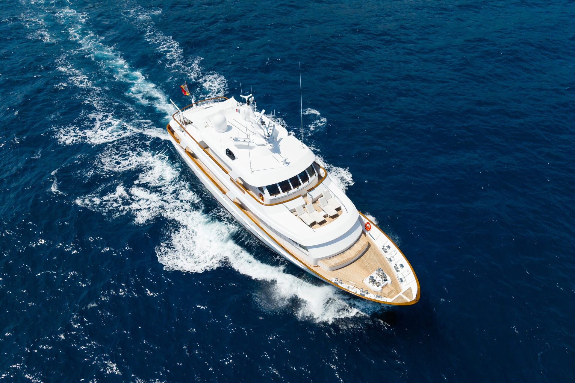 A large white luxury yacht cruises through deep blue ocean water, leaving a foamy wake behind it on a sunny day.
