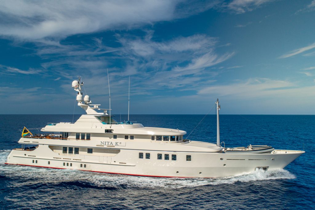 A large white luxury yacht named NITA K II cruises on calm blue ocean waters under a partly cloudy sky.