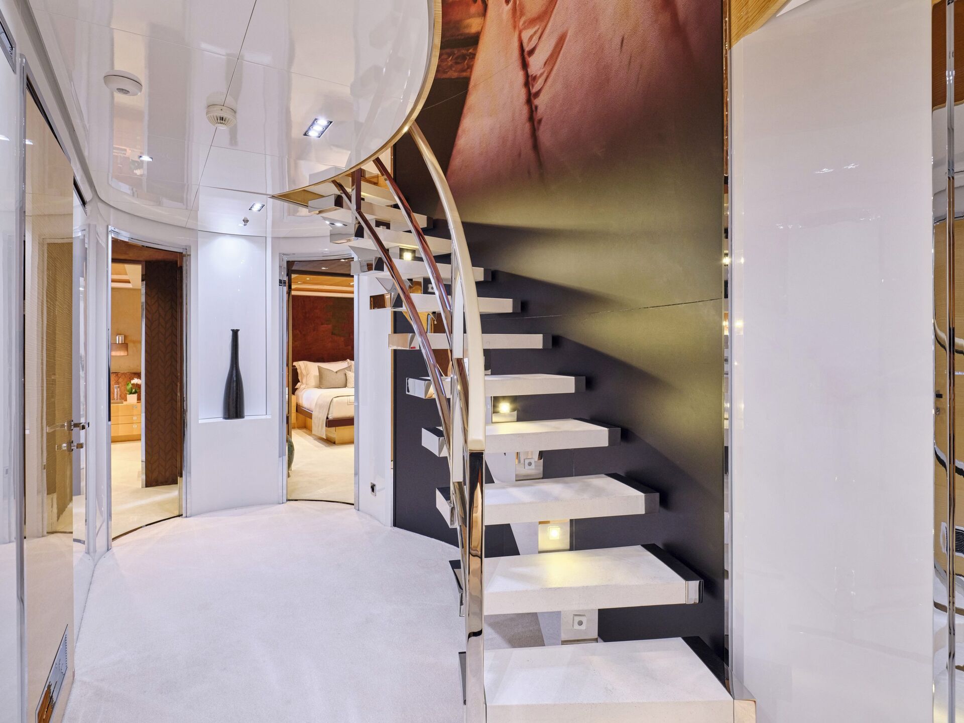 A modern, spiral staircase with floating white steps and metal railings leads to an upper floor in a sleek, contemporary interior with glossy walls and a cozy bedroom visible in the background.