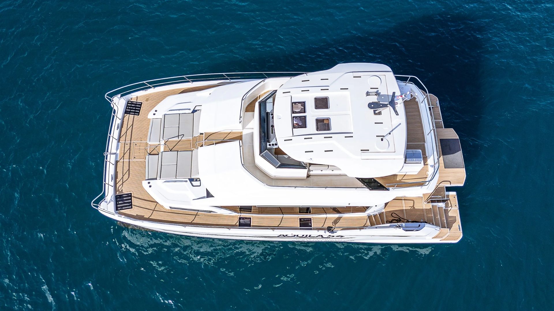 Aerial view of a white luxury yacht with outdoor seating areas and sunbeds on blue water, showing the deck, railings, and the yacht’s sleek design.