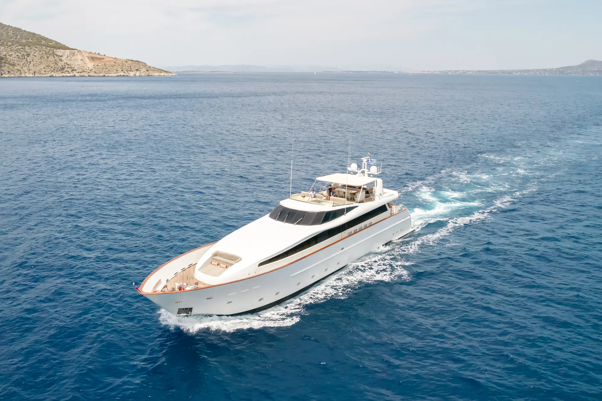 A large white yacht cruises through calm blue waters near a rocky coastline under a clear sky.
