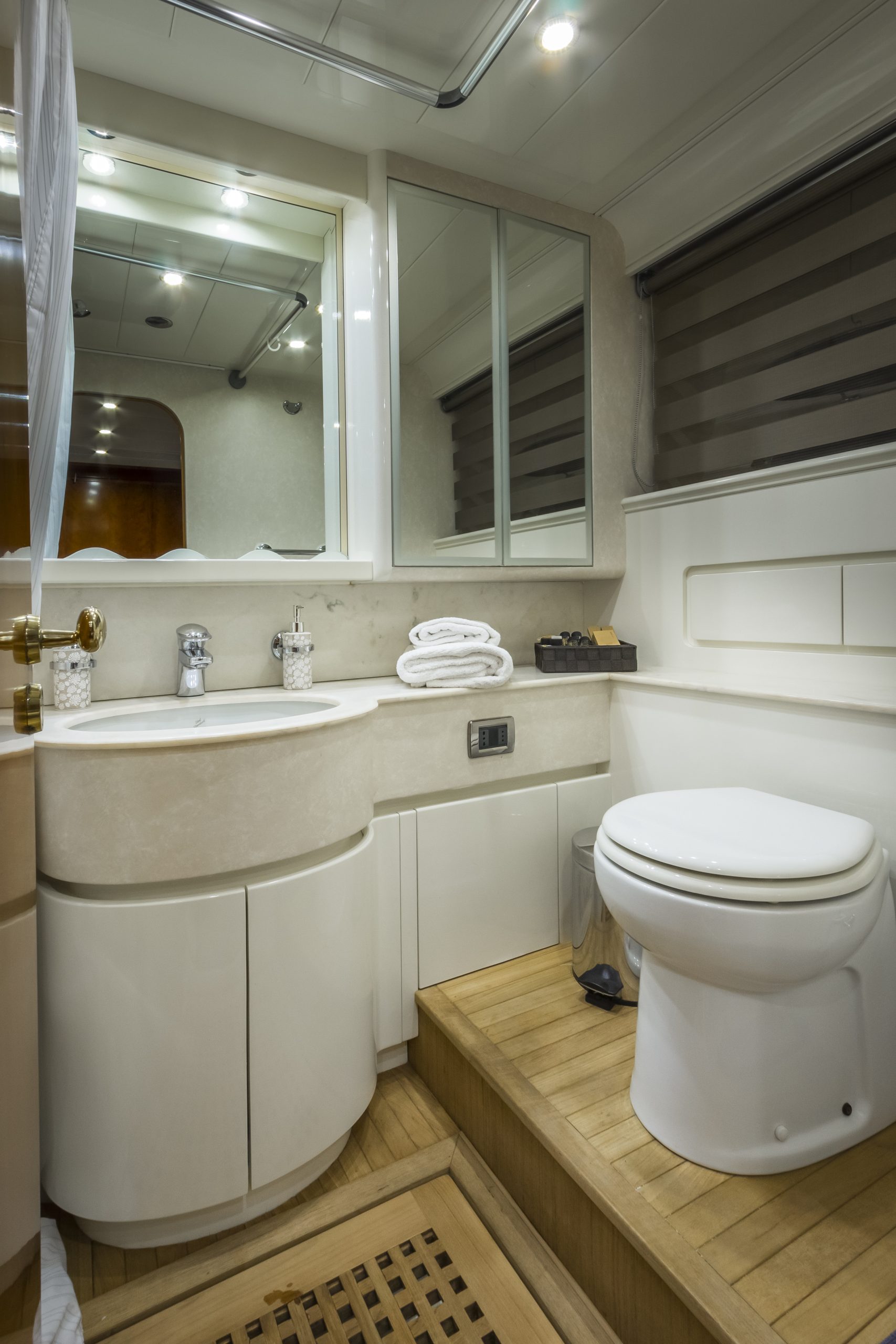 AMORAKI Modern bathroom with a white toilet, curved sink cabinet, large mirror, stacked towels, and wood-style flooring. Overhead lights illuminate the space, which has a clean and compact design.