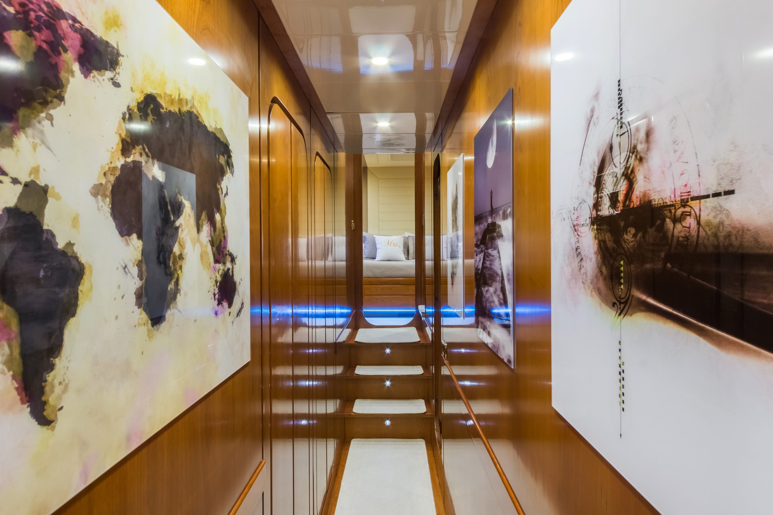 A polished hallway with wooden walls, steps leading up to a bright bedroom, and large abstract artwork featuring a world map and a ship on the walls.