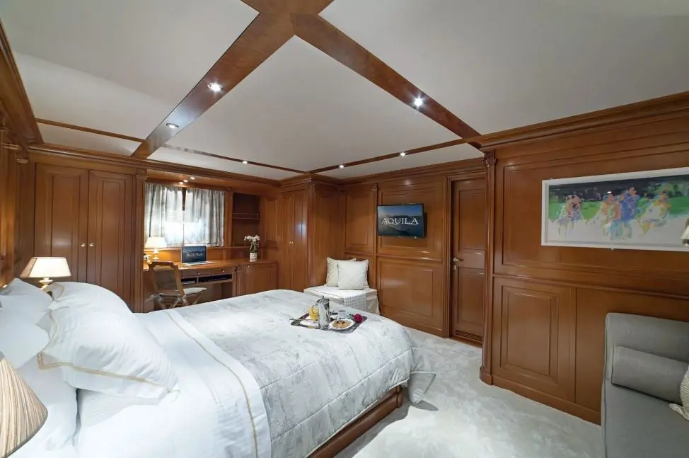 A luxurious bedroom with wood-paneled walls, a large bed with white bedding, a breakfast tray on the bed, a desk with a chair, artwork on the wall, and soft lighting creating a cozy atmosphere.
