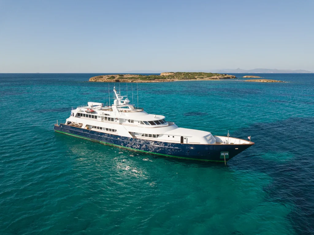 A large luxury yacht is anchored in clear turquoise water near a small, green island under a clear blue sky.
