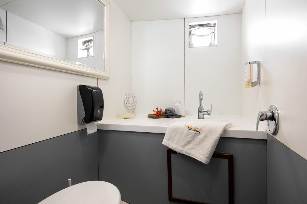 ABORDA A modern bathroom with white and gray walls, a mirror, a sink with a towel, a soap dispenser, a black paper towel holder, and a small window above the sink letting in light.