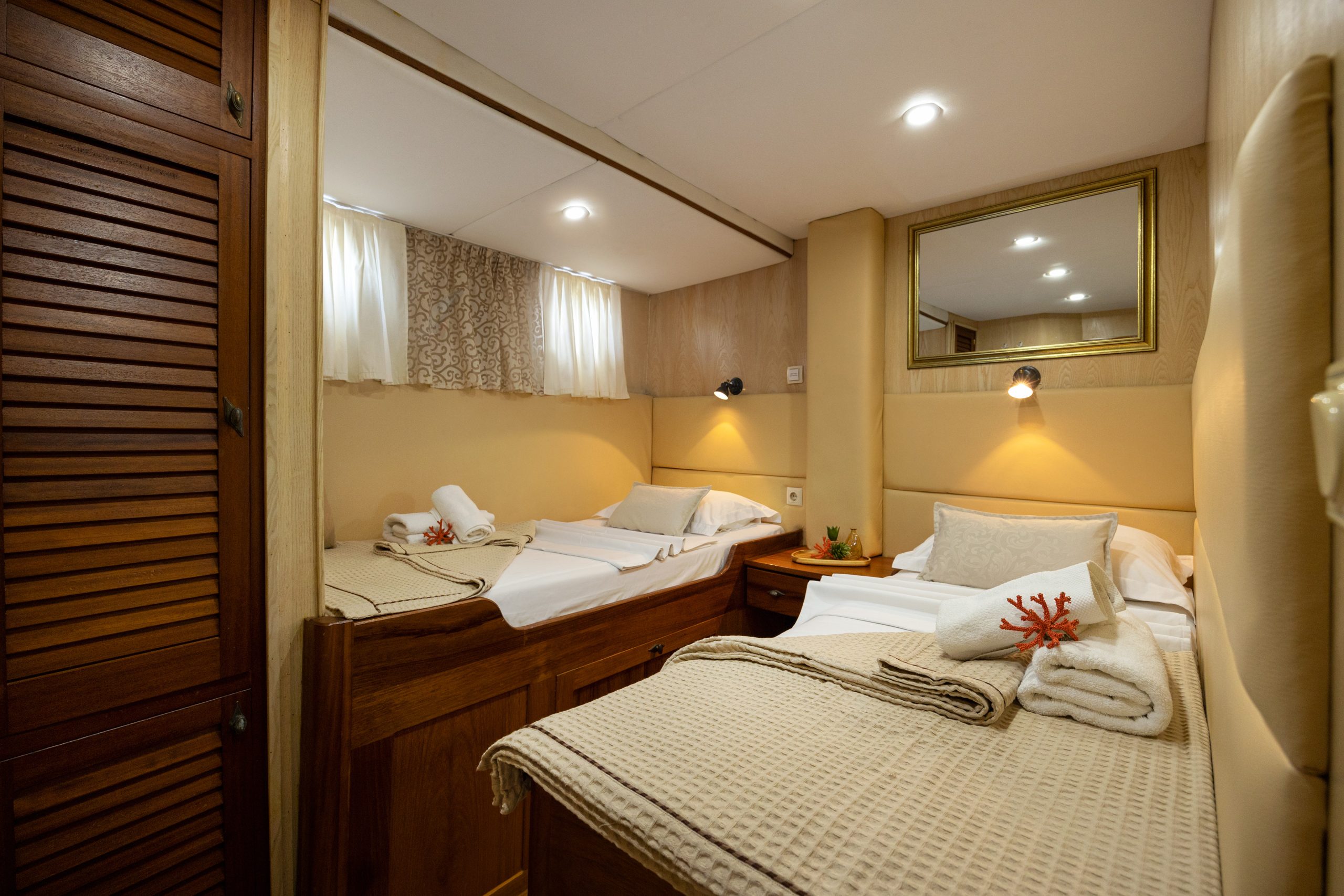 ABORDA Cozy cabin room with two single beds, beige bedding, rolled towels, wall lamps, a mirror above one bed, a small nightstand, and a wooden wardrobe. Soft lighting creates a warm, inviting atmosphere.