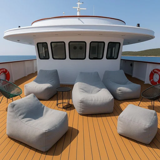 Sun deck of a yacht with modern gray bean bag chairs, a small round table, and two metal chairs. The deck has a wood-like finish, and the background shows the ocean and distant shoreline under a clear sky.