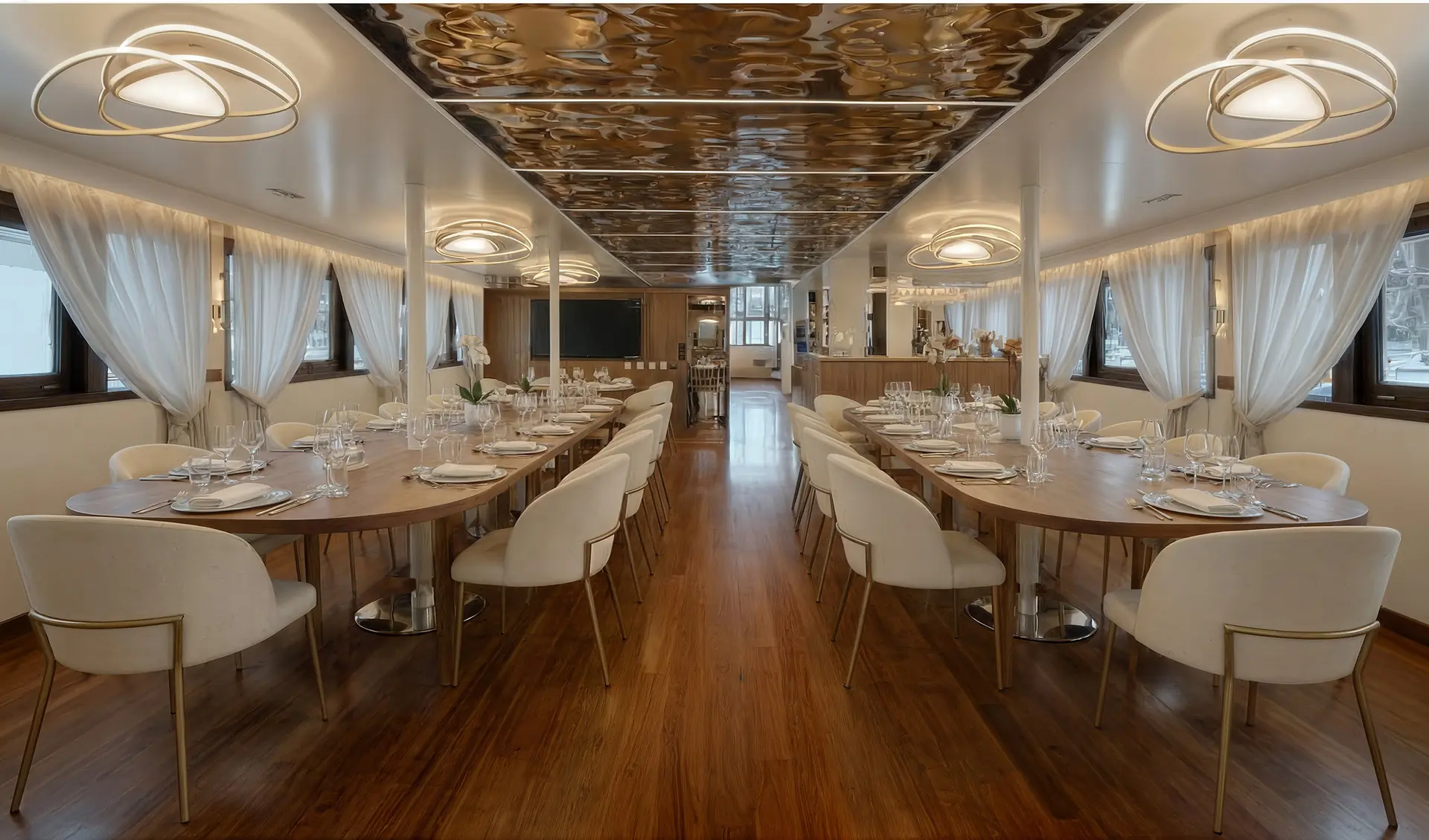 Elegant dining room with two long wooden tables, white cushioned chairs, modern pendant lights, wood flooring, large windows with sheer curtains, and a polished reflective ceiling. The room is set for a formal meal.