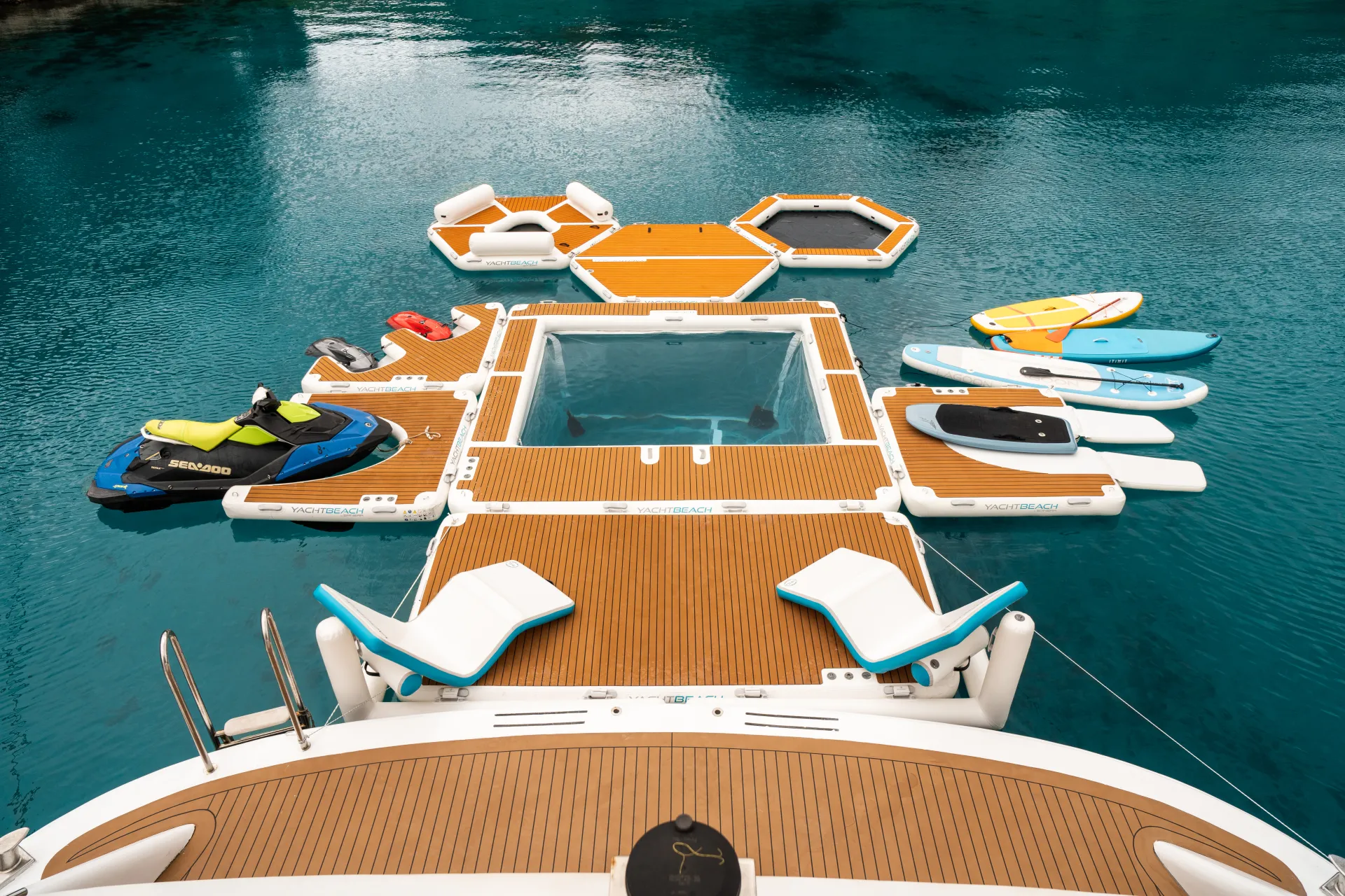 CRISTAL A luxury yacht deck extends over clear blue water, featuring floating platforms, lounge chairs, paddleboards, and a jet ski, creating a spacious, modular aquatic relaxation area.