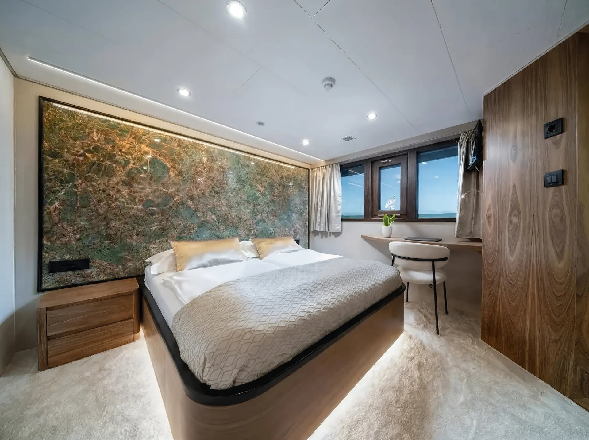 A modern bedroom with a large bed, textured green and brown accent wall, soft lighting, wooden furniture, two windows with curtains, a chair by a built-in desk, and a plush beige carpet.