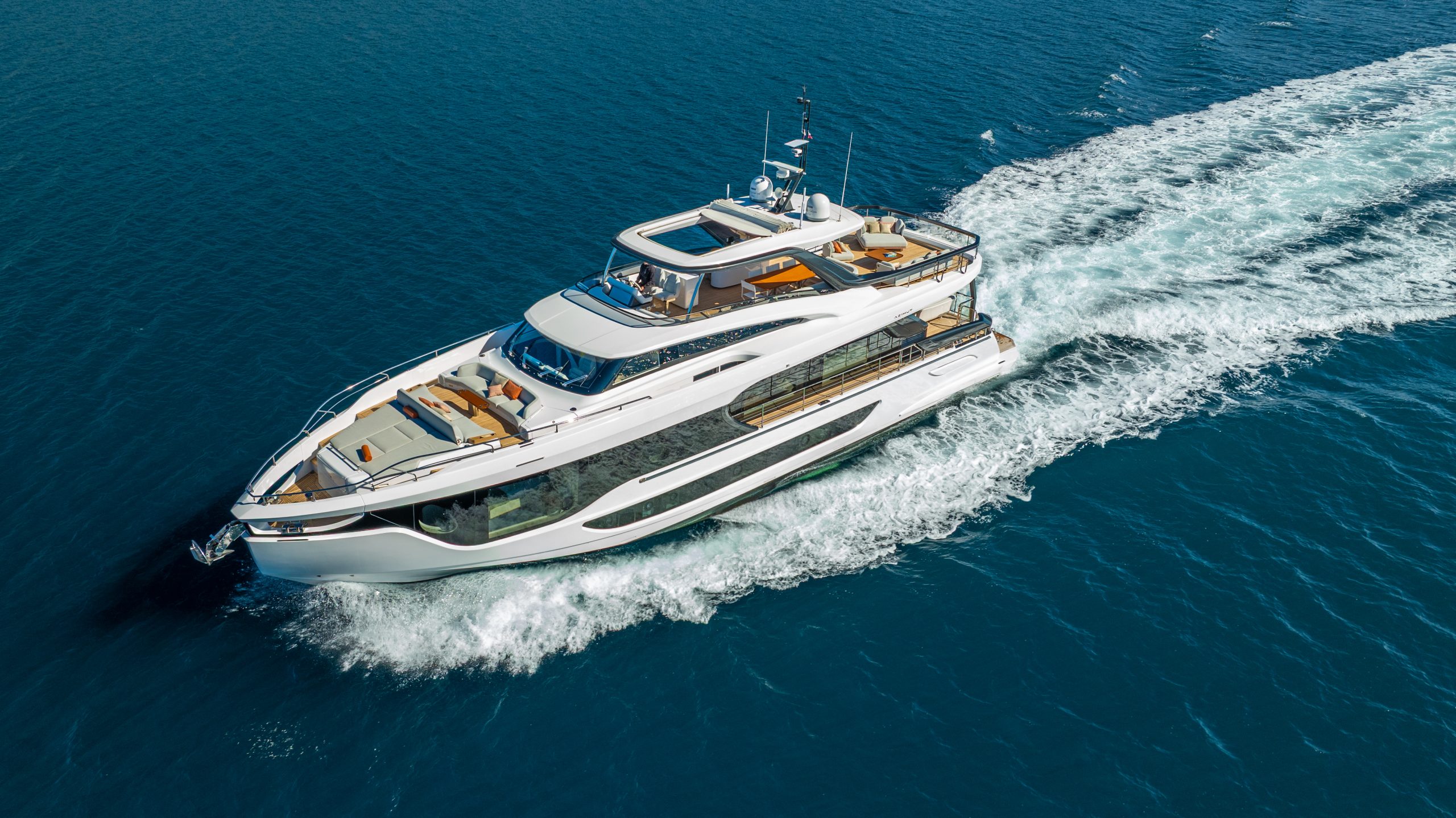 VIVA II A luxurious white yacht cruises through calm blue ocean waters, leaving a foamy wake behind. The yacht features multiple decks with seating areas and sun loungers, and is surrounded by clear, open sea.