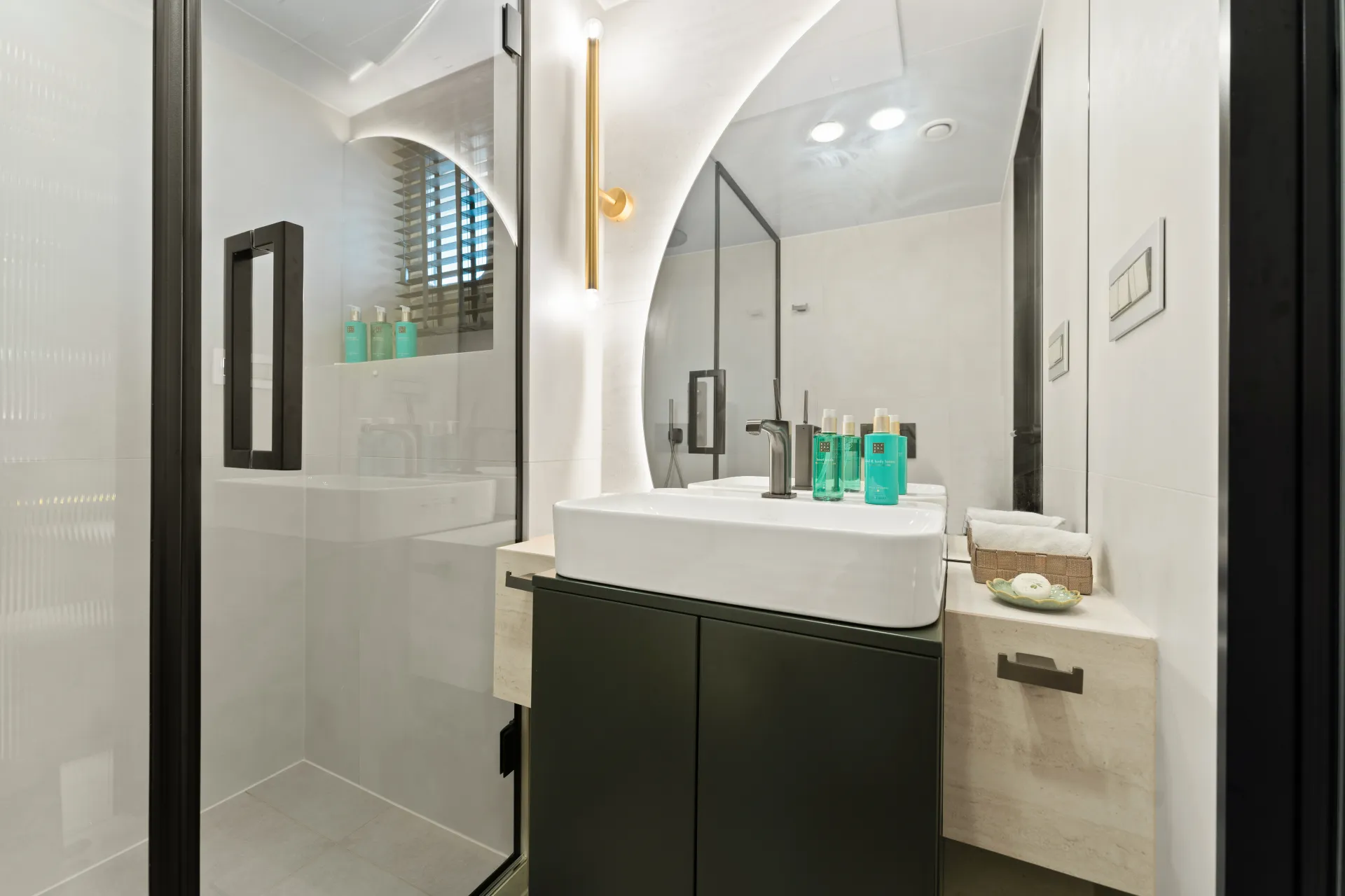 MAXITA Modern bathroom with a large mirror, square white sink on a dark vanity, glass shower enclosure, and toiletries on the counter; neutral color palette with bright lighting and minimalist decor.
