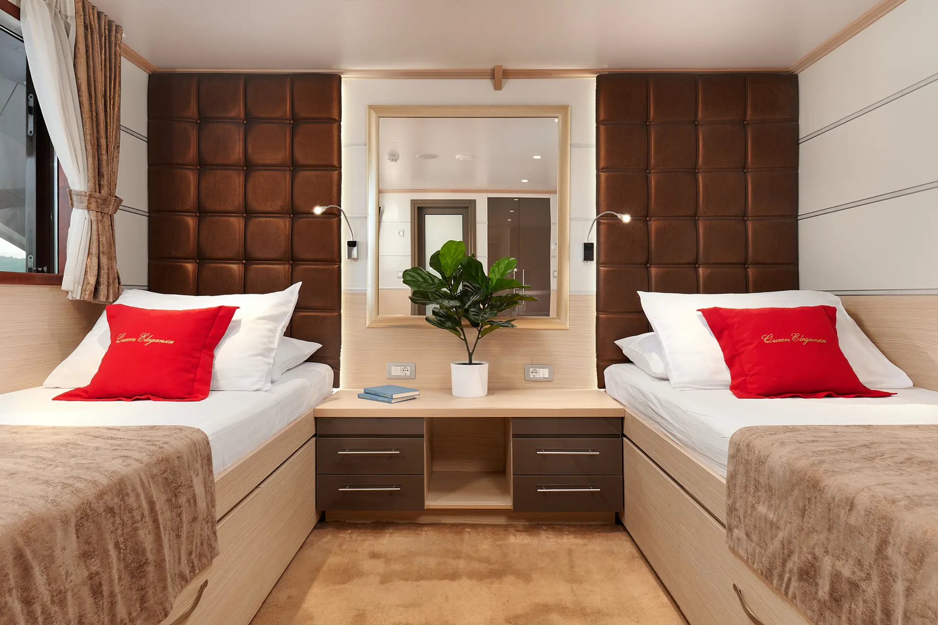 Modern bedroom with two single beds, red accent pillows, a plant, and a large mirror above a nightstand, reflecting the opposite side of the room. Neutral tones and soft lighting create a cozy atmosphere.