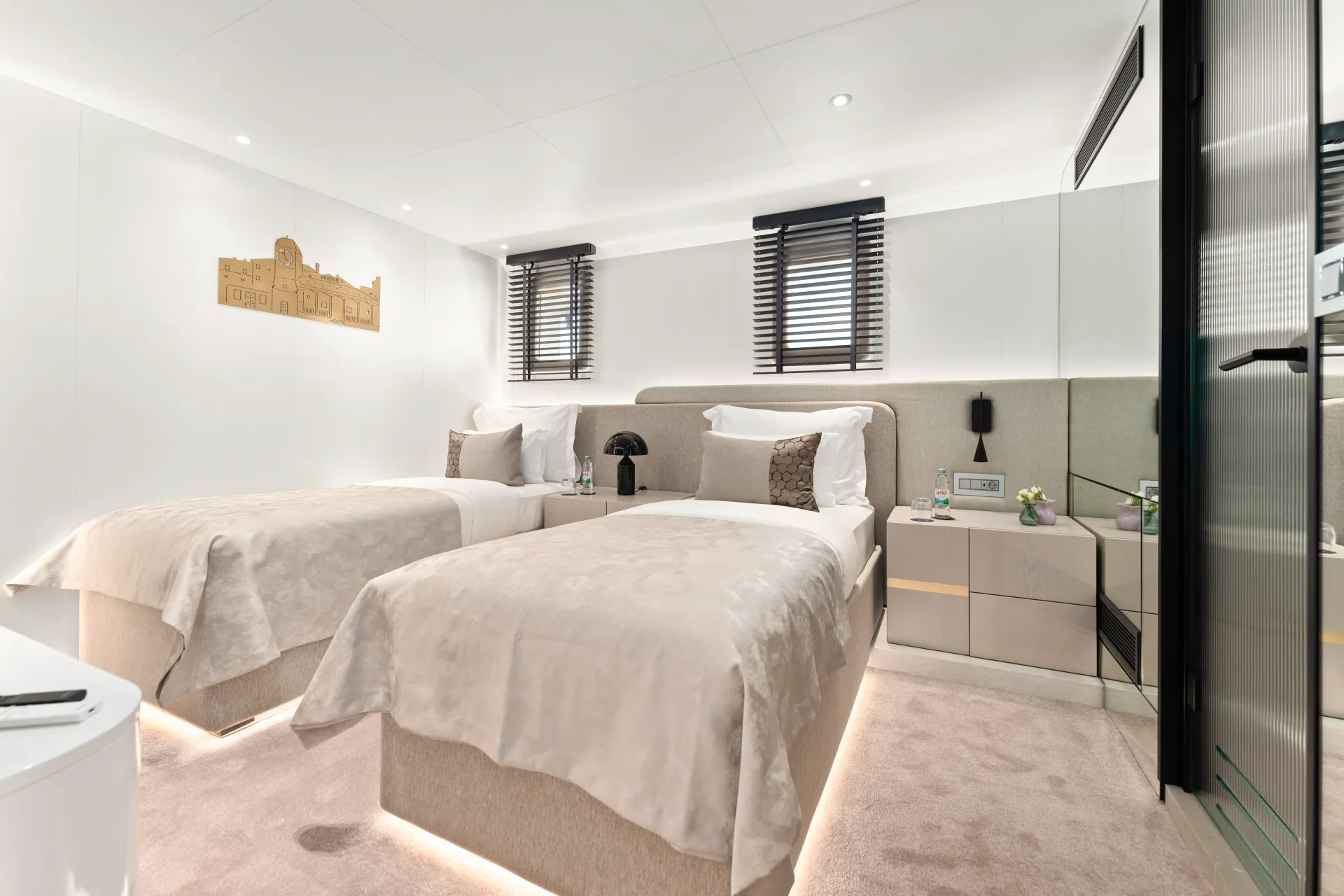 MAXITA A modern hotel room with two single beds, beige bedding, built-in nightstands, and minimalist decor. There are two windows with dark blinds, a wall art piece, and soft ambient lighting under the beds.