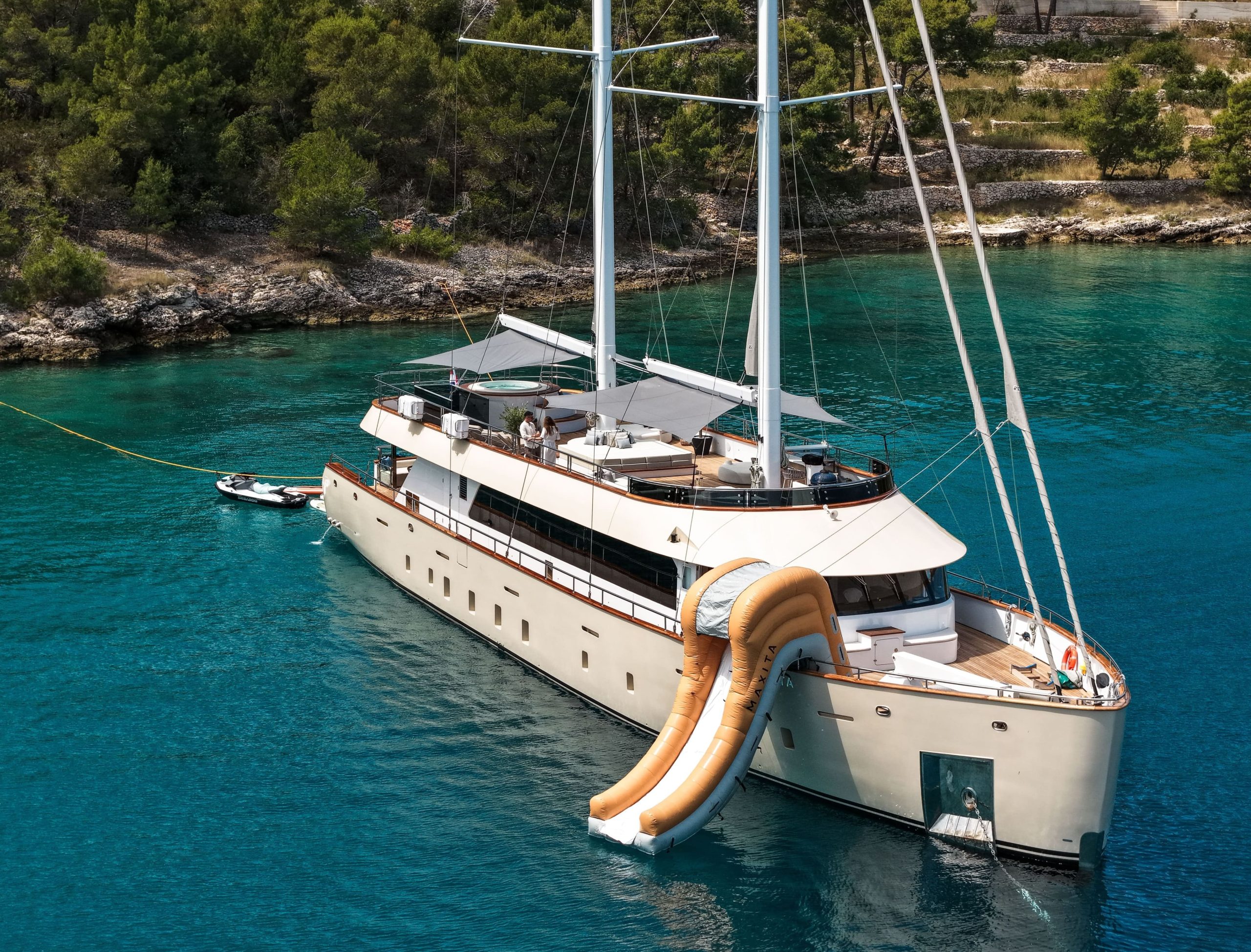 Large yacht anchored in a turquoise bay with an inflatable slide attached to the side.