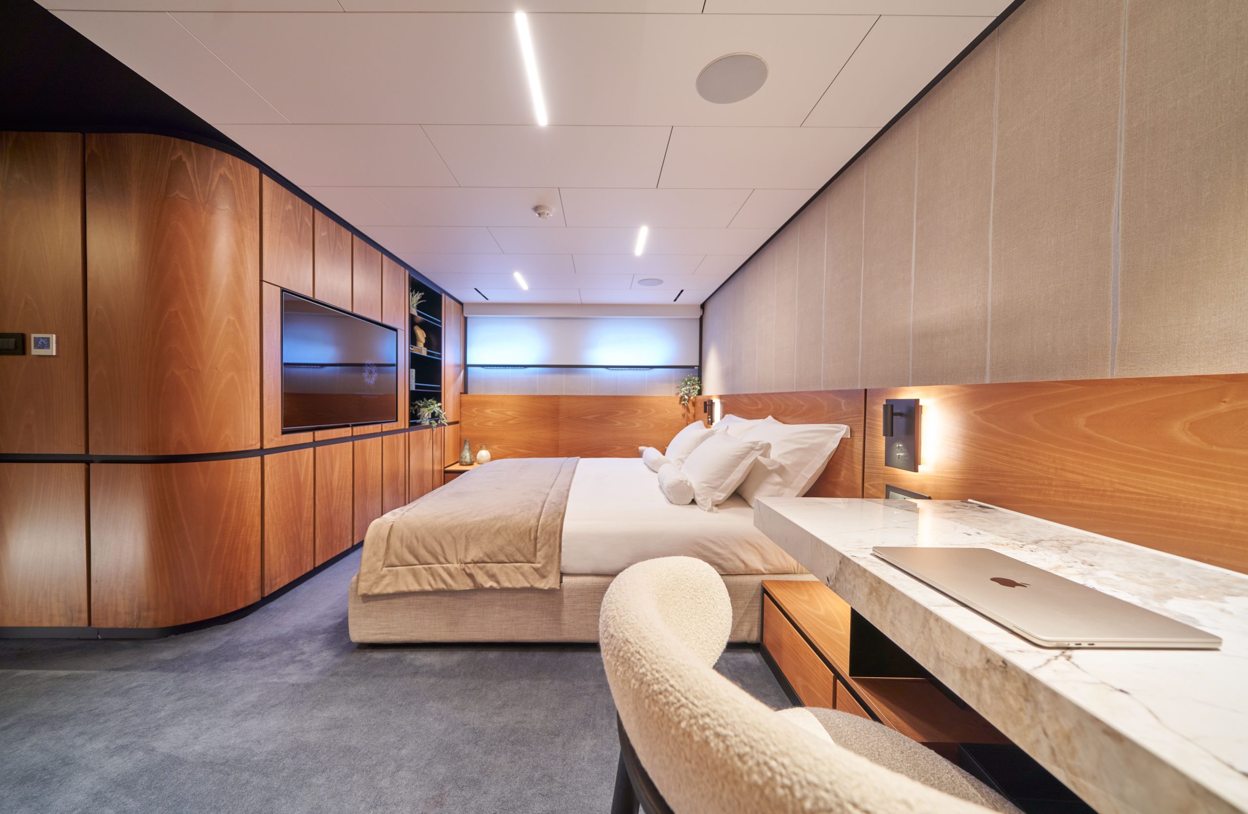 MARALLURE A modern, luxurious bedroom with wood-paneled walls, a large bed with white bedding, a marble desk with a laptop, built-in shelves, and soft ambient lighting.