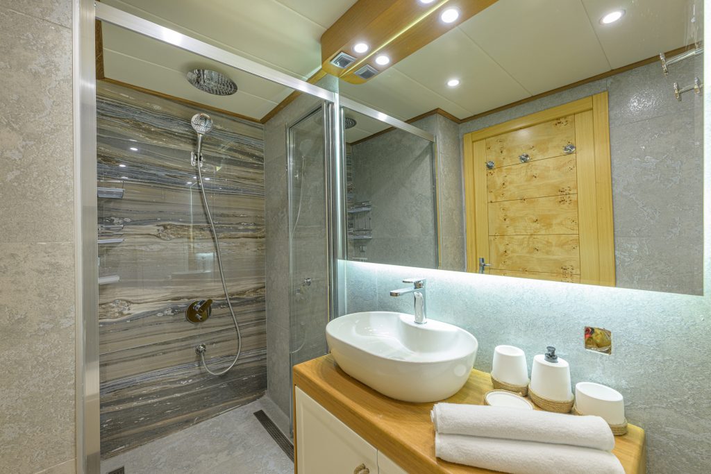 Modern bathroom with a glass-enclosed shower, rain showerhead, striped tile walls, vessel sink on a wooden countertop, rolled white towels, and a large mirror above the sink.