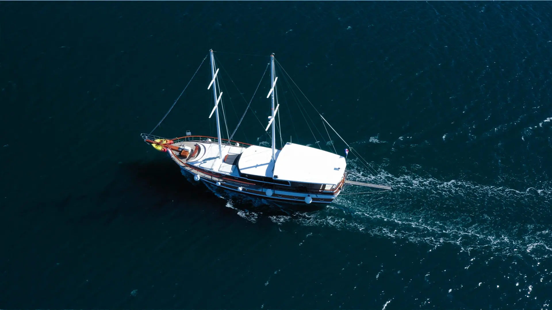 A single sailboat with white sails cruises on deep blue water, leaving a small wake behind it.