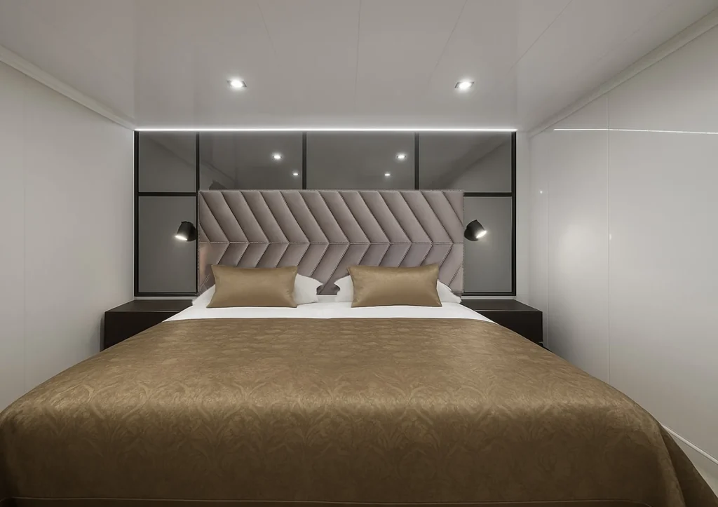 PREMIER A modern, minimalist bedroom with a large bed featuring a geometric padded headboard, two gold pillows, a gold bedspread, black bedside tables, wall-mounted lamps, and a black-framed glass wall behind the bed.