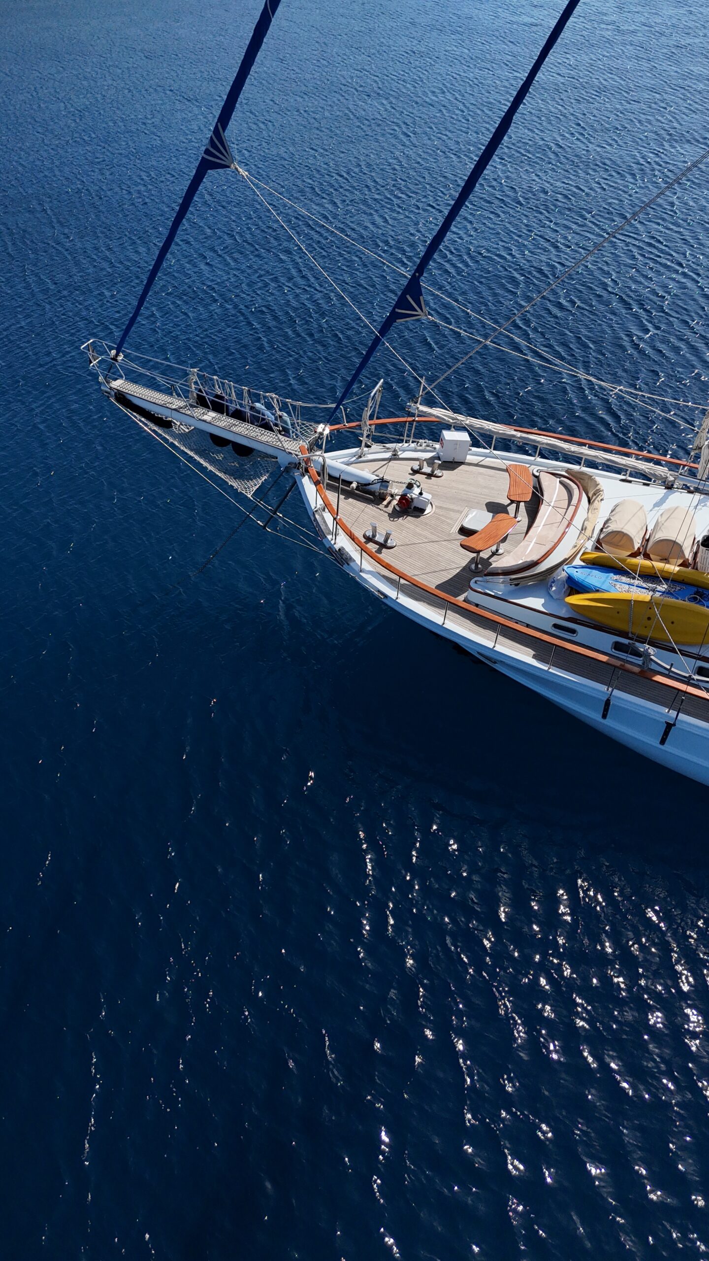 CEMRE 4 Aerial view of the front deck of a sailboat with lounge chairs, yellow kayaks, and equipment, floating on calm, deep blue water.