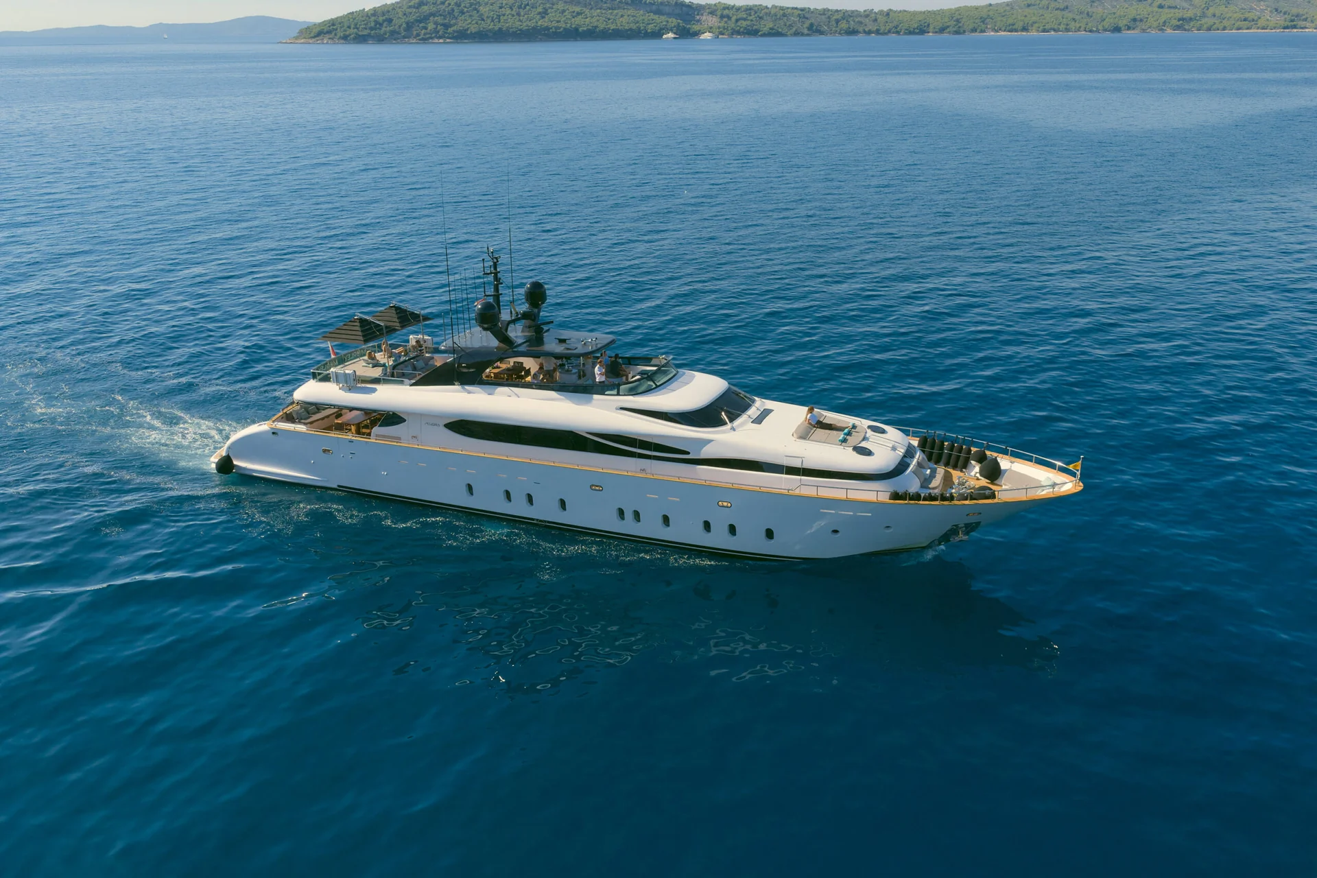 A white motor yacht cruising across open blue water toward a distant island.