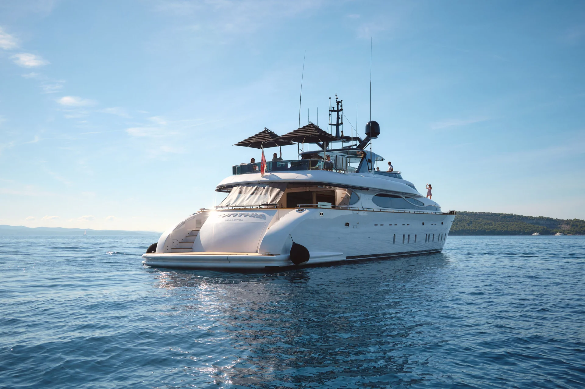 A large white motor yacht cruising on the open sea with people visible on its decks.
