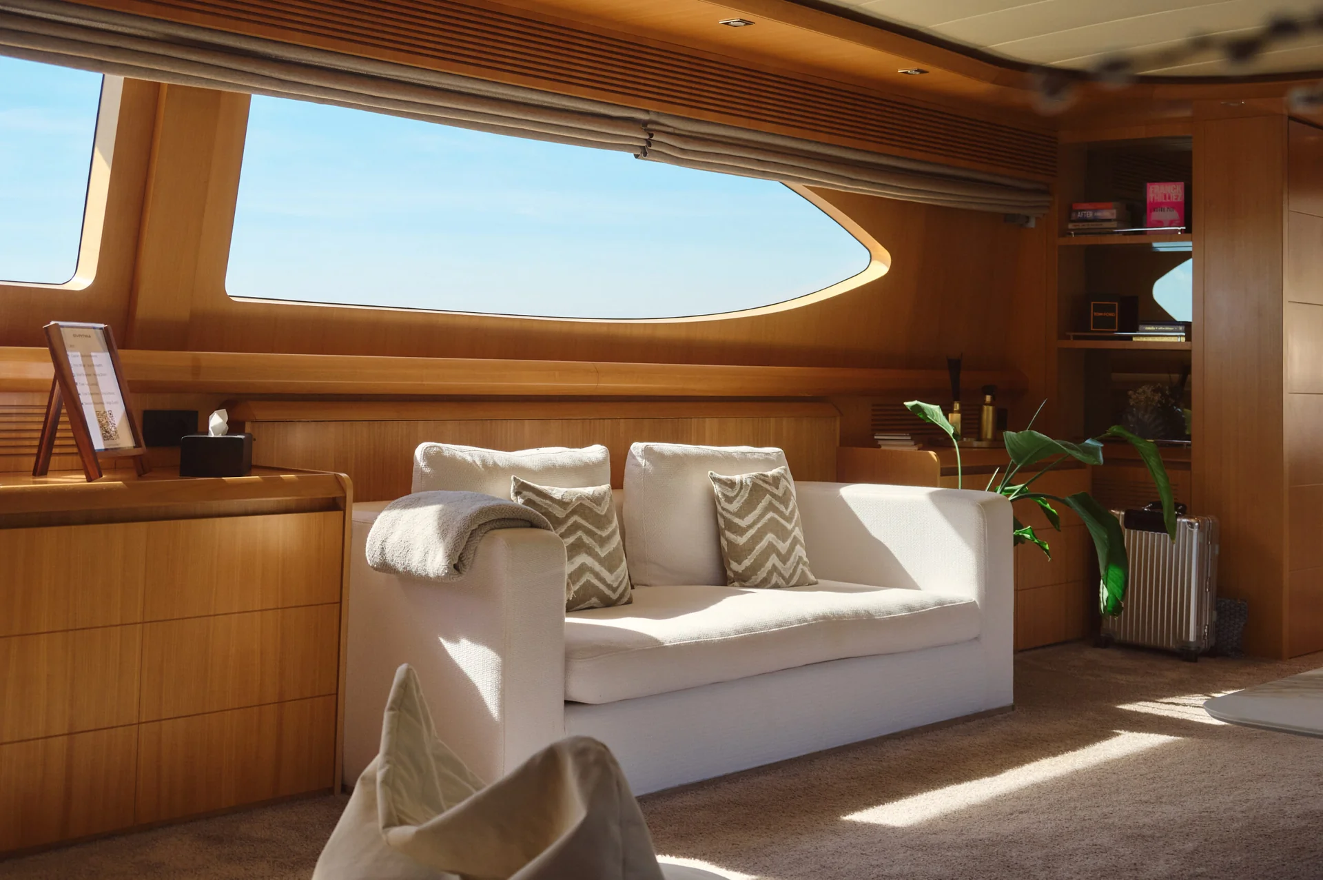 A white sofa with patterned pillows sits in a wood-paneled room with a large window overlooking the ocean.