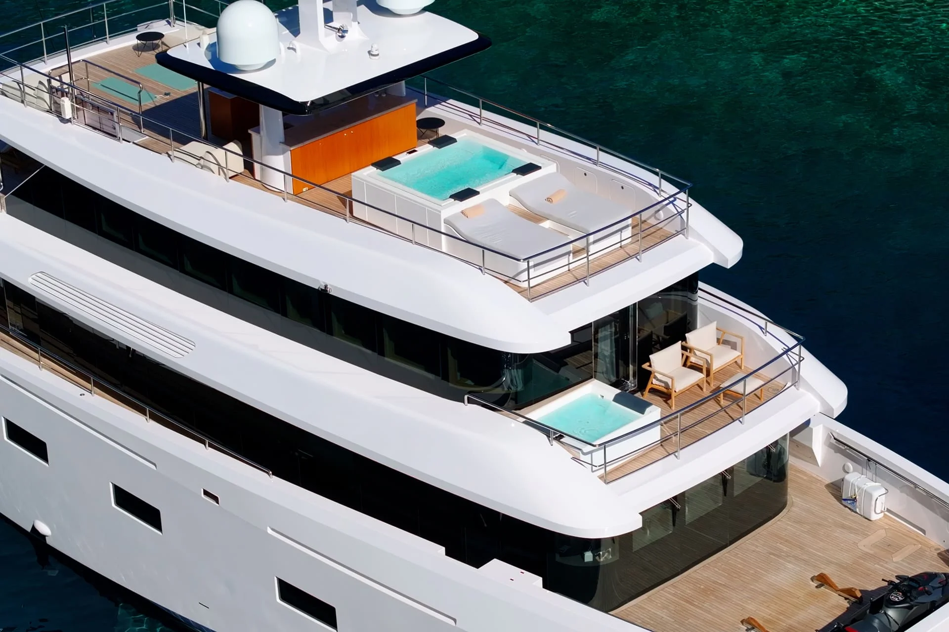 A luxury white yacht floats on clear turquoise water, featuring multiple decks with pools, sun loungers, and outdoor seating areas.