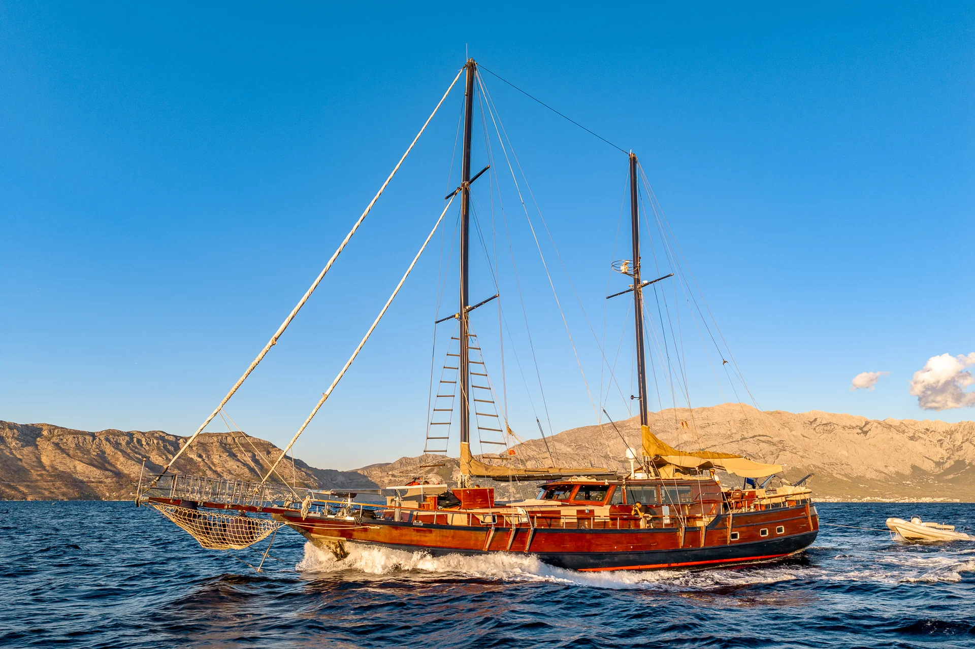PACHA A wooden schooner sailing on the water with mountains in the background.